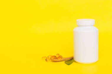 Omega-3 kapsülleri yeşil yapraklı arka planda beyaz bir şişede yatar. Balık yağı tabletleri. Biyolojik olarak aktif katkı maddeleri. Omega 6, Omega 9, A vitamini, E, D vitamini, D3 vitamini..