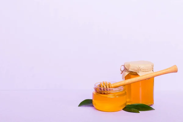 Honey in jar with leaves and honey dipper on colored background top view with copy text.