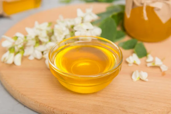 Sweet honey jar surrounded spring acacia blossoms. Honey flows from a spoon in a jar. jars of clear fresh acacia honey on wooden background.