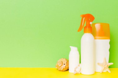 Plaj aksesuarları. Yazın UVB cilt koruması için nemlendirici güneş kremi şişesi ve renkli arka planda deniz kabukları. Kopyalama alanı kullan.