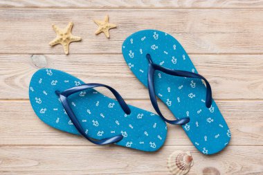 Renkli arka planda parmak arası terlikleri ve deniz kabuğu olan düz bir kompozisyon. Metin üstü görünümü için boşluk.