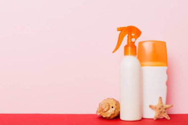 Plaj aksesuarları. Yazın UVB cilt koruması için nemlendirici güneş kremi şişesi ve renkli arka planda deniz kabukları. Kopyalama alanı kullan.