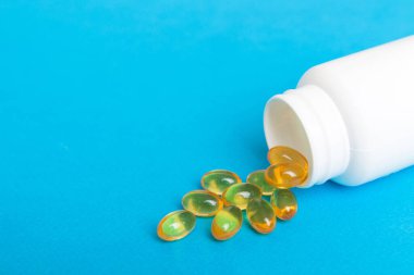 Omega-3 kapsülleri masa arkasında beyaz bir şişede yatıyor. Balık yağı tabletlerinin üst görüntüsü. Biyolojik olarak aktif katkı maddeleri. omega 6, omega 9, A vitamini, D vitamini, D3 vitamini, akşam çuha çiçeği yağı.