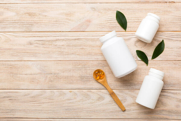 Капсулы Омега-3 лежат в белой бутылке на столе на зеленом фоне листьев. Таблетки из рыбьего масла. Биологически активные добавки. омега 6, омега 9, витамин А, Е, D, витамин D3 вид сверху с местом для копирования.