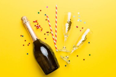 Gözlüklü bir şişe şampanya ve renkli arka planda renkli konfeti. Üst görünüm yatıyordu.