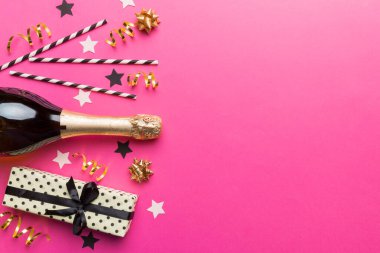 Gözlüklü bir şişe şampanya ve renkli arka planda renkli konfeti. Üst görünüm yatıyordu.