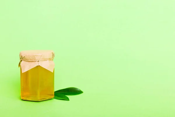 Honey in jar with leaves and honey dipper on colored background top view with copy text.