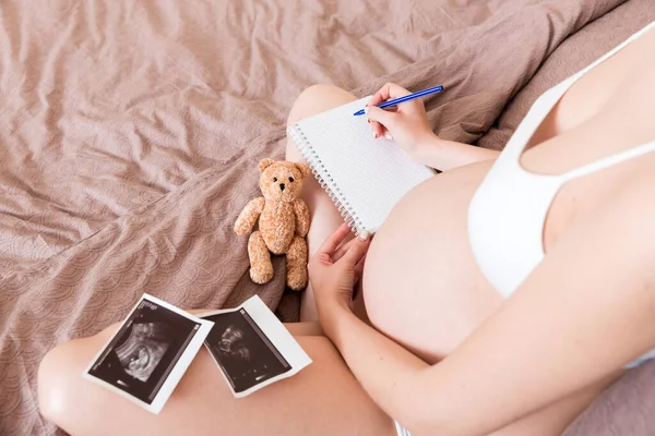 Top view caring future mother writing diary with ultrasound. pregnant woman tummy making notes feeling during pregnancy or creating scrapbook.
