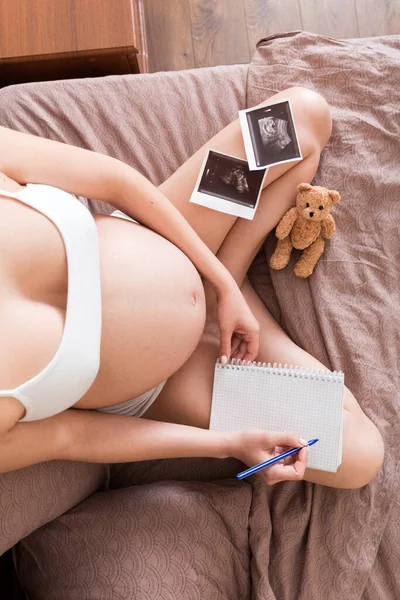 Top view caring future mother writing diary with ultrasound. pregnant woman tummy making notes feeling during pregnancy or creating scrapbook.