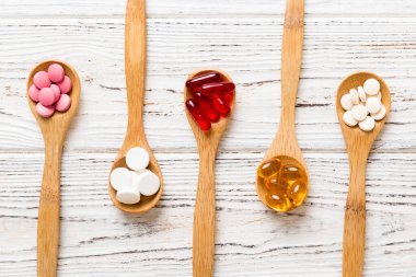Renkli bir arka planda kaşıkta vitamin kapsülleri. Haplar sağlıklı bir yemek olarak sunuldu. Kırmızı yumuşak jel vitamin takviye kapsülleri kaşık üzerinde.