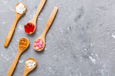 Renkli bir arka planda kaşıkta vitamin kapsülleri. Haplar sağlıklı bir yemek olarak sunuldu. Kırmızı yumuşak jel vitamin takviye kapsülleri kaşık üzerinde.