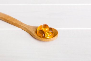 Renkli bir arka planda kaşıkta vitamin omega kapsülleri. Haplar sağlıklı bir yemek olarak sunuldu. Kırmızı yumuşak jel vitamin takviye kapsülleri kaşık üzerinde.