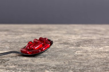 Renkli bir arka planda kaşıkta vitamin kapsülleri. Haplar sağlıklı bir yemek olarak sunuldu. Kırmızı yumuşak jel vitamin takviye kapsülleri kaşık üzerinde.