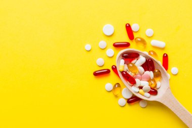Renkli bir arka planda kaşıkta vitamin kapsülleri. Haplar sağlıklı bir yemek olarak sunuldu. Kırmızı yumuşak jel vitamin takviye kapsülleri kaşık üzerinde.