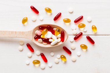 Renkli bir arka planda kaşıkta vitamin kapsülleri. Haplar sağlıklı bir yemek olarak sunuldu. Kırmızı yumuşak jel vitamin takviye kapsülleri kaşık üzerinde.