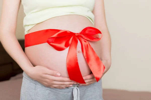 Bauch Einer Schwangeren Frau Mit Roter Schleife Vor Heimischem Hintergrund — Stockfoto