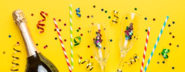 Gözlüklü bir şişe şampanya ve renkli arka planda renkli konfeti. Üst görünüm yatıyordu.