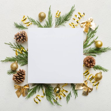 Noel kompozisyonu düzdü. Kare kağıt boş, çam ağacı dalları, renkli arka planda noel süslemeleri. Üst görünüm, metin için boşluk kopyala.