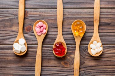 Renkli bir arka planda kaşıkta vitamin kapsülleri. Haplar sağlıklı bir yemek olarak sunuldu. Kırmızı yumuşak jel vitamin takviye kapsülleri kaşık üzerinde.
