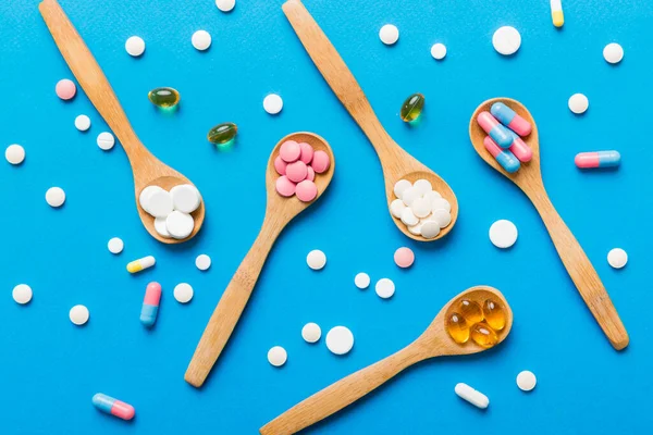 Vitamin capsules in a spoon on a colored background. Pills served as a healthy meal. Red soft gel vitamin supplement capsules on spoon.