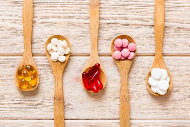 Renkli bir arka planda kaşıkta vitamin kapsülleri. Haplar sağlıklı bir yemek olarak sunuldu. Kırmızı yumuşak jel vitamin takviye kapsülleri kaşık üzerinde.