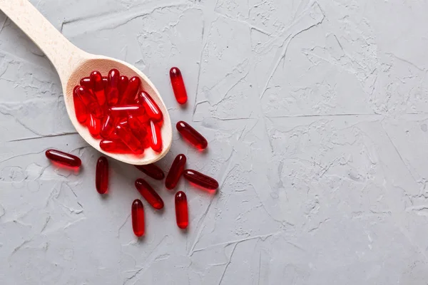 Vitamin capsules in a spoon on a colored background. Pills served as a healthy meal. Red soft gel vitamin supplement capsules on spoon.