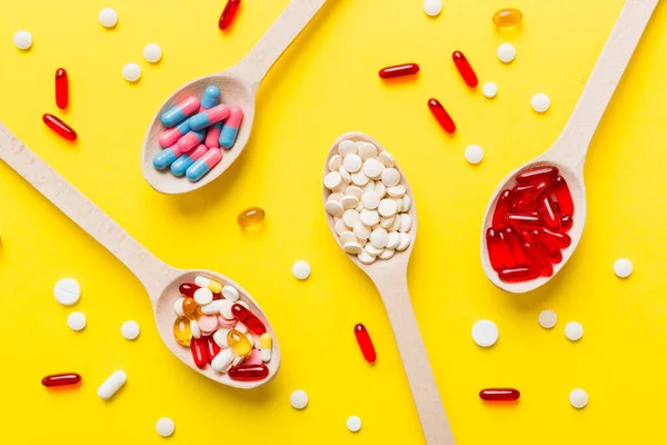 Vitamin capsules in a spoon on a colored background. Pills served as a healthy meal. Red soft gel vitamin supplement capsules on spoon.