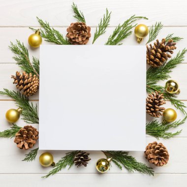 Noel kompozisyonu düzdü. Kare kağıt boş, çam ağacı dalları, renkli arka planda noel süslemeleri. Üst görünüm, metin için boşluk kopyala.