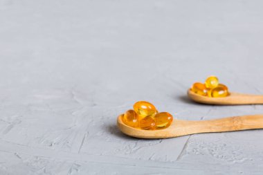 Vitamin omega capsules in a spoon on a colored background. Pills served as a healthy meal. Red soft gel vitamin supplement capsules on spoon.