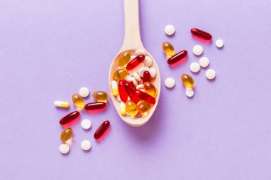Renkli bir arka planda kaşıkta vitamin kapsülleri. Haplar sağlıklı bir yemek olarak sunuldu. Kırmızı yumuşak jel vitamin takviye kapsülleri kaşık üzerinde.