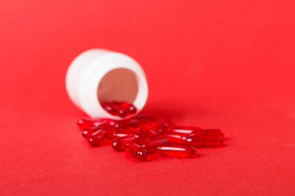 Red pills spilled around a pill bottle. Medicines and prescription pills flat lay background. Red medical capsules.