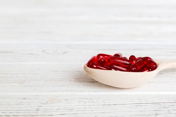 Vitamin capsules in a spoon on a colored background. Pills served as a healthy meal. Red soft gel vitamin supplement capsules on spoon.