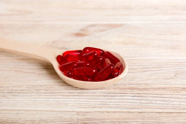 Vitamin capsules in a spoon on a colored background. Pills served as a healthy meal. Red soft gel vitamin supplement capsules on spoon.