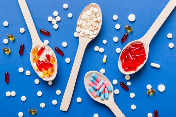 Vitamin capsules in a spoon on a colored background. Pills served as a healthy meal. Red soft gel vitamin supplement capsules on spoon.