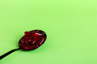 Renkli bir arka planda kaşıkta vitamin kapsülleri. Haplar sağlıklı bir yemek olarak sunuldu. Kırmızı yumuşak jel vitamin takviye kapsülleri kaşık üzerinde.
