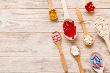Renkli bir arka planda kaşıkta vitamin kapsülleri. Haplar sağlıklı bir yemek olarak sunuldu. Kırmızı yumuşak jel vitamin takviye kapsülleri kaşık üzerinde.