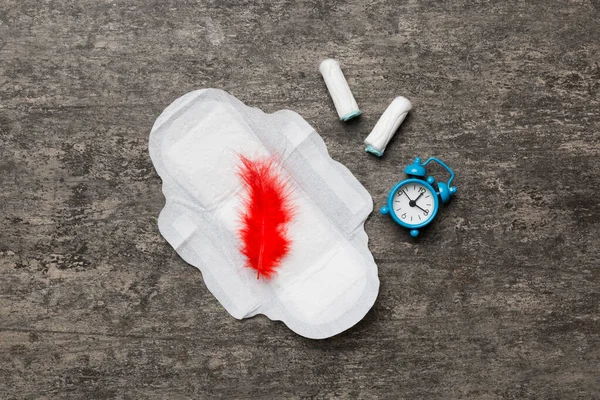 Ringing alarm clock with sanitary female tampons and menstrual sanitary pads. Medical concept of woman critical days and menstruation. Female daily hygiene. Copy space.