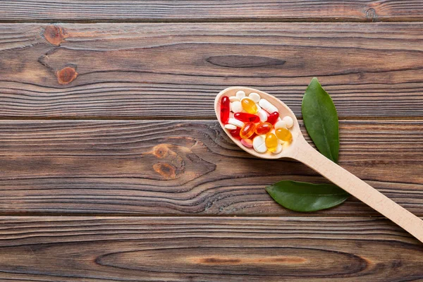 Vitamin capsules in a spoon on a colored background. Pills served as a healthy meal. Red soft gel vitamin supplement capsules on spoon.