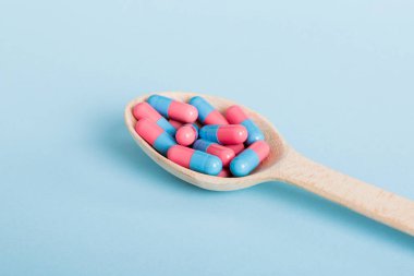 Renkli bir arka planda kaşıkta vitamin kapsülleri. Haplar sağlıklı bir yemek olarak sunuldu. Kırmızı yumuşak jel vitamin takviye kapsülleri kaşık üzerinde.