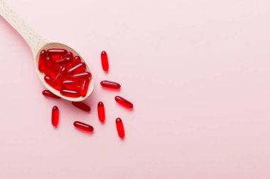 Renkli bir arka planda kaşıkta vitamin kapsülleri. Haplar sağlıklı bir yemek olarak sunuldu. Kırmızı yumuşak jel vitamin takviye kapsülleri kaşık üzerinde.