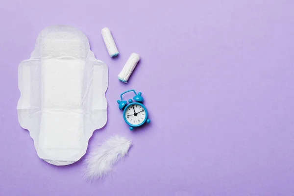 Ringing alarm clock with sanitary female tampons and menstrual sanitary pads. Medical concept of woman critical days and menstruation. Female daily hygiene. Copy space.