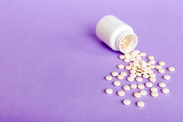 Medicine bottle and white pills spilled on a light background. Medicines and prescription pills flat lay background. White medical pills and tablets spilling out of a drug bottle.