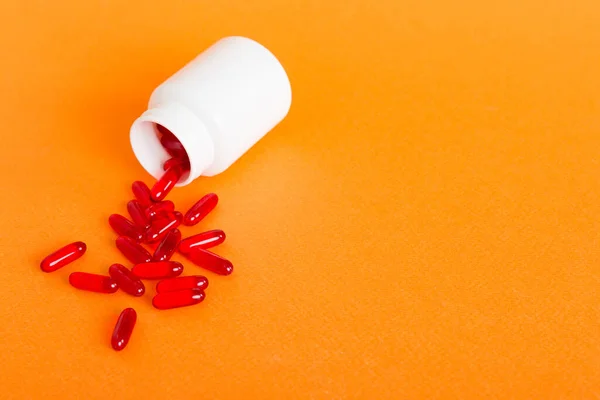 Red pills spilled around a pill bottle. Medicines and prescription pills flat lay background. Red medical capsules.