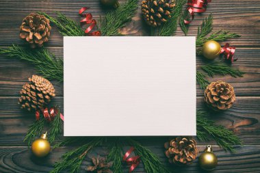 Noel kompozisyonu düzdü. Kare kağıt boş, çam ağacı dalları, renkli arka planda noel süslemeleri. Üst görünüm, metin için boşluk kopyala.