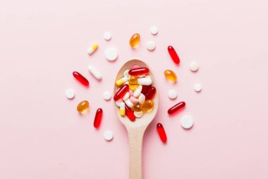 Renkli bir arka planda kaşıkta vitamin kapsülleri. Haplar sağlıklı bir yemek olarak sunuldu. Kırmızı yumuşak jel vitamin takviye kapsülleri kaşık üzerinde.