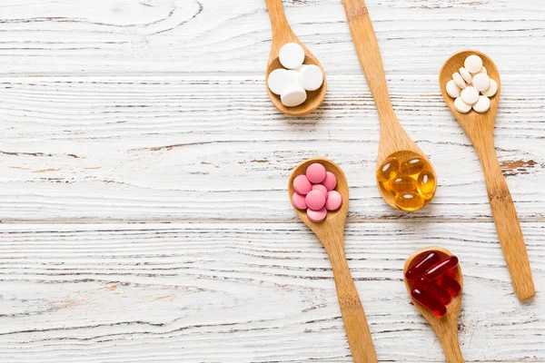 Vitamin capsules in a spoon on a colored background. Pills served as a healthy meal. Red soft gel vitamin supplement capsules on spoon.