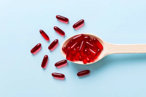 Vitamin capsules in a spoon on a colored background. Pills served as a healthy meal. Red soft gel vitamin supplement capsules on spoon.