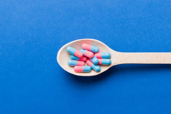 Vitamin capsules in a spoon on a colored background. Pills served as a healthy meal. Red soft gel vitamin supplement capsules on spoon.