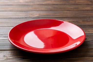 Ahşap zemindeki boş kırmızı tabağın perspektif görüntüsü. Tasarımın için boş boşluk.