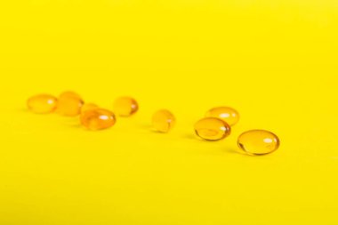 Heap of yellov pills on colored background. Tablets scattered on a table. Pile of red soft gelatin capsule. Vitamins and dietary supplements concept.